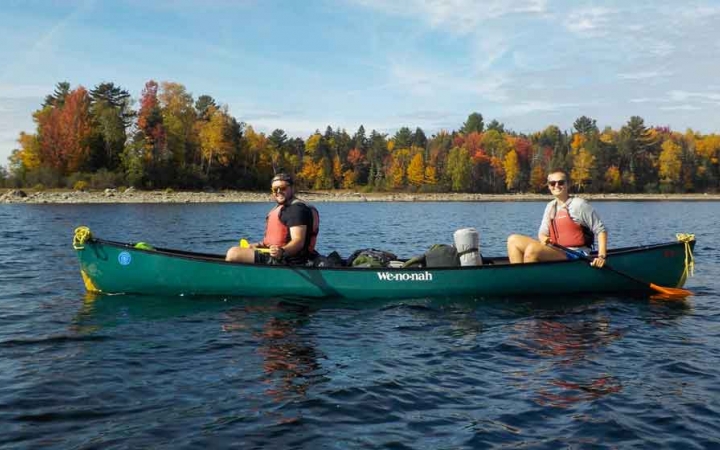 two people paddle a canoe with fall foliage on the shore in the background on an outward bound expedition in maine